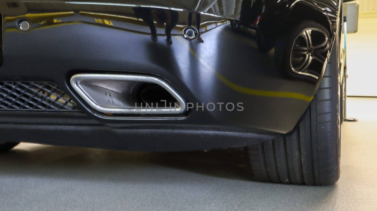 Square tailpipe at the rear right side of a black sports car. Very low plan. The rear bumper, wheel and tailpipe of the packed vehicle are smoke- and gas-free