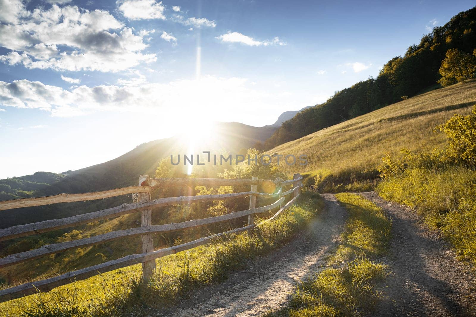 beautiful landscape scenery with hillside green country road and wooden fence at sunset with blue sky above