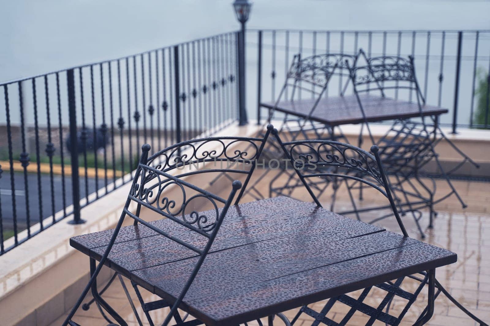 closeup detail of black iron metal chairs near wooden table with rain drops on rainy outdoor restaurant terrace
