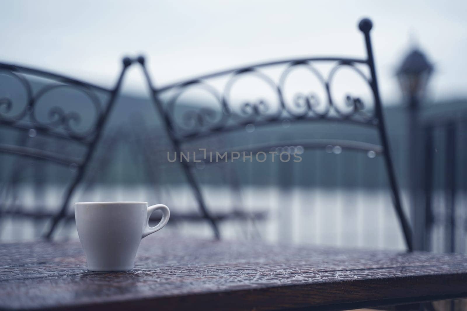 closeup detail of white small espresso coffee cup on wooden table with rain drops on rainy outdoor restaurant terrace