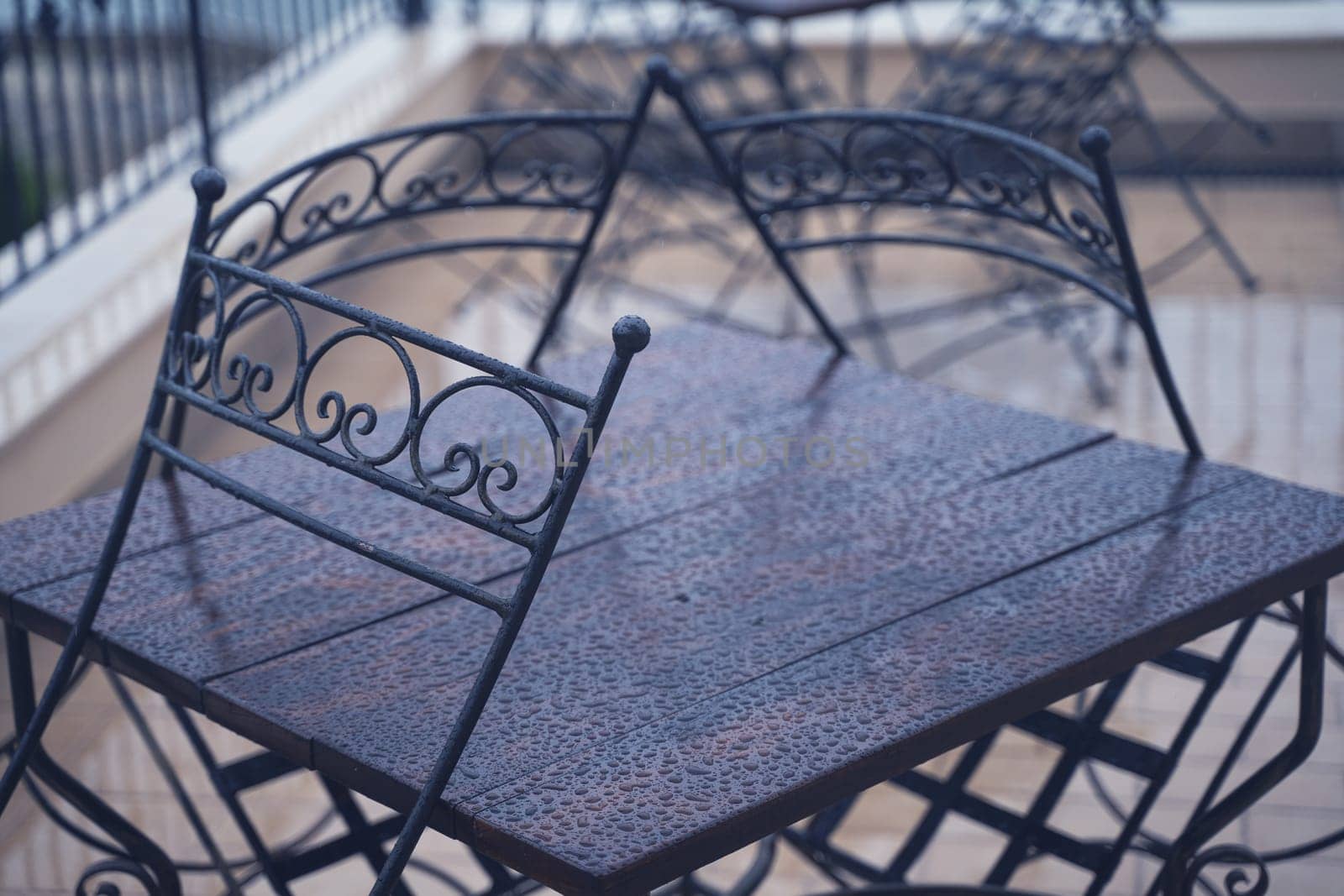 closeup detail of black iron metal chairs near wooden table with rain drops on rainy outdoor restaurant terrace