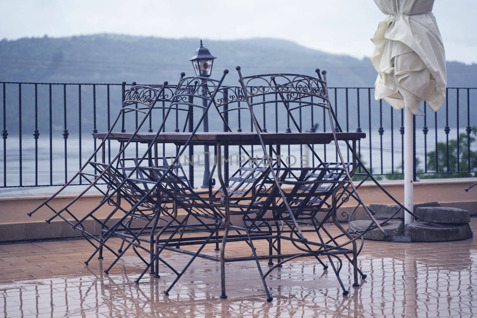 closeup detail of black iron metal chairs near wooden table with rain drops on rainy outdoor restaurant terrace
