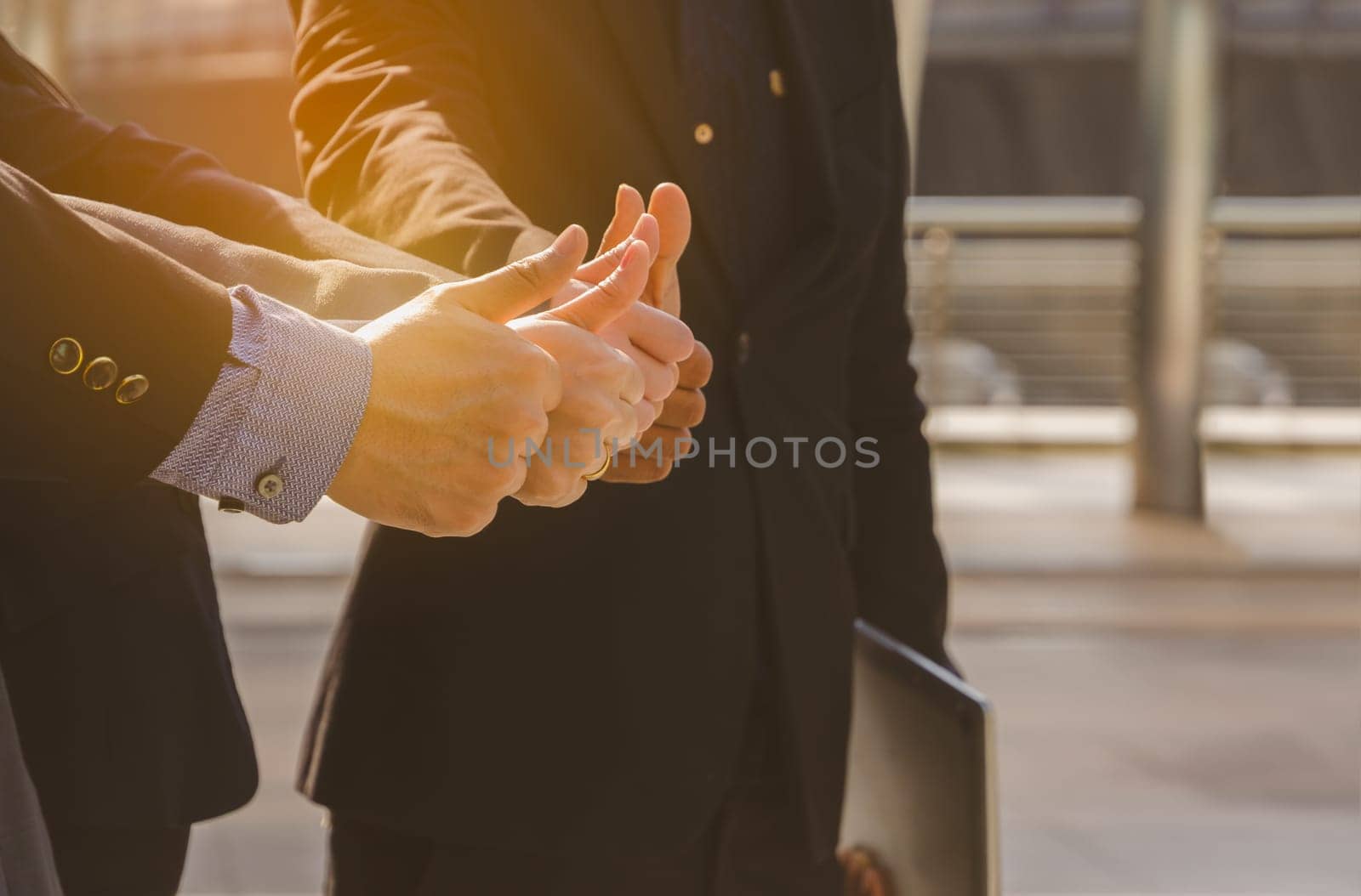 Business people team in black suits standing in city outdoors and showing thumbs up, one of them holding laptop. Teamwork, cooperation and business successful concept