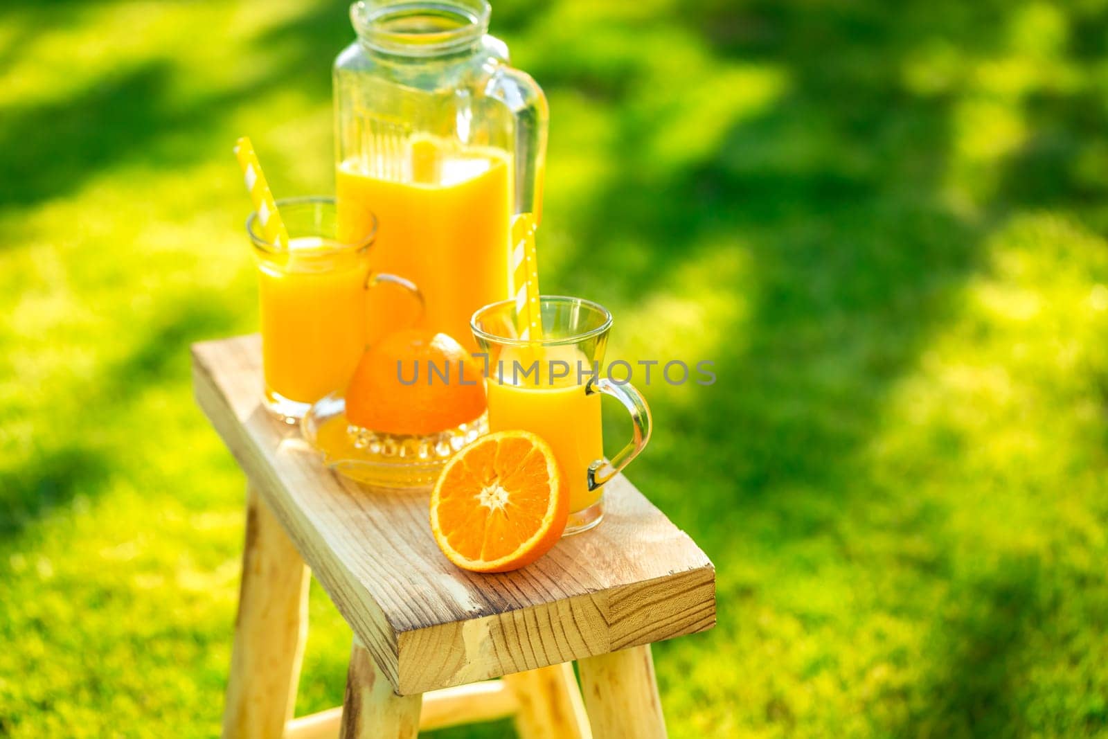Two glasses of tasty freshly squeezed orange juice on garden stool on green lawn