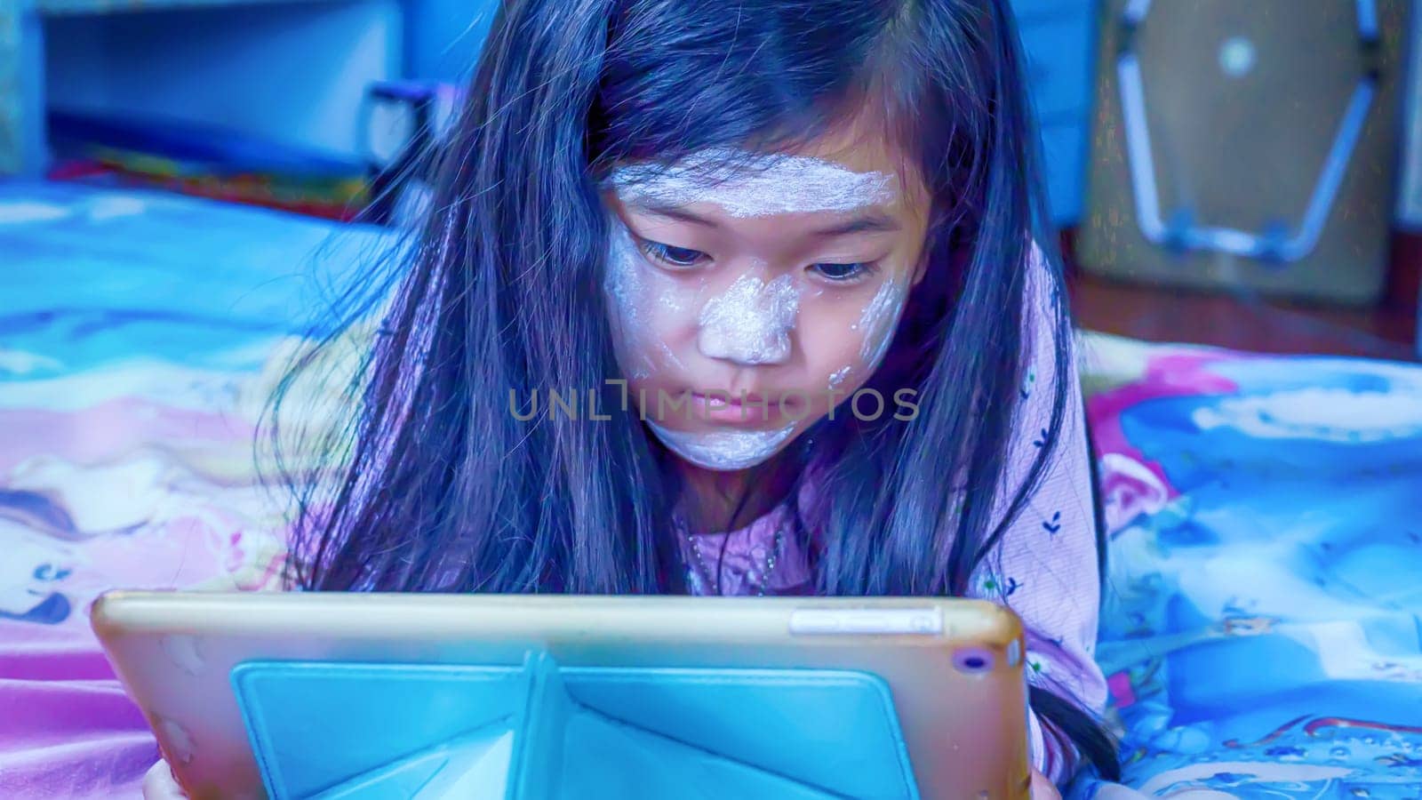 The children are playing tablet on the bed.