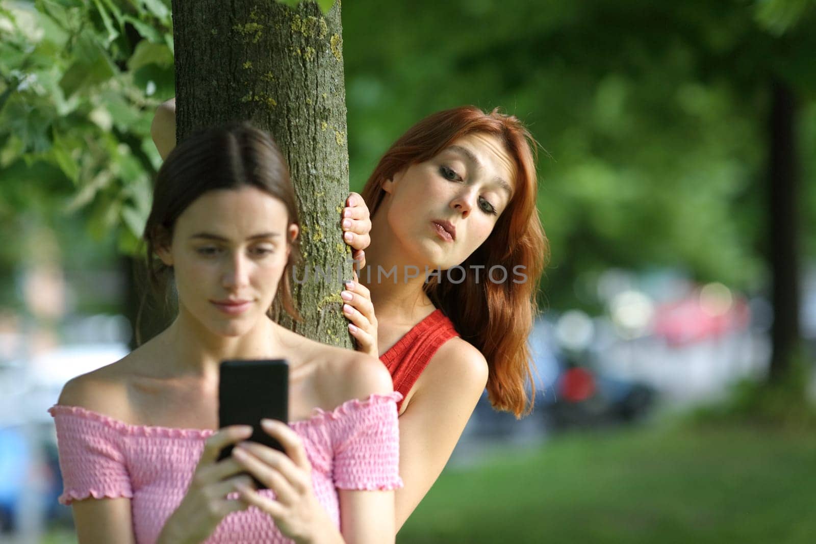 Woman using phone being spied by her friend