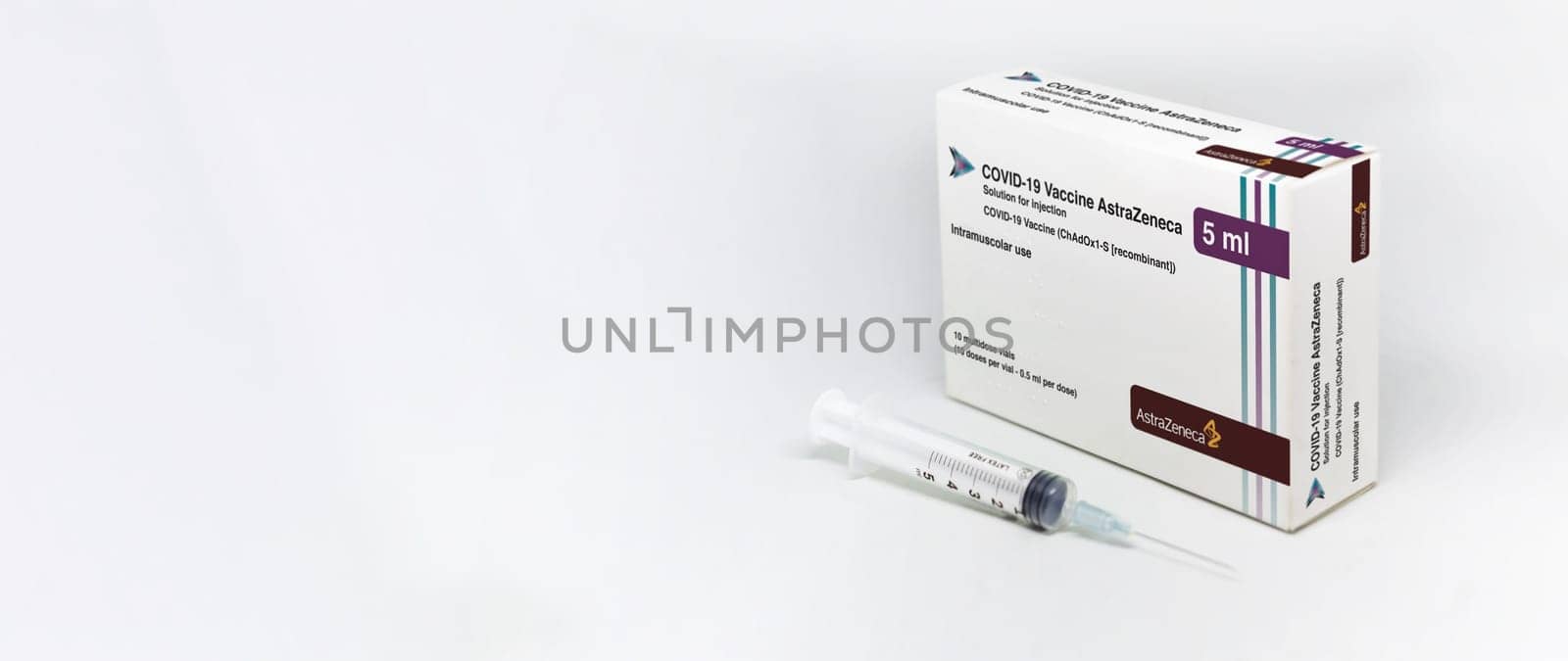 Cambridge, UK, february 5th 2021: A syringe next to the AstraZeneca Covid-19 Vaxzevria vaccine box isolated on a white background. Health and prevention. Copy space and banner