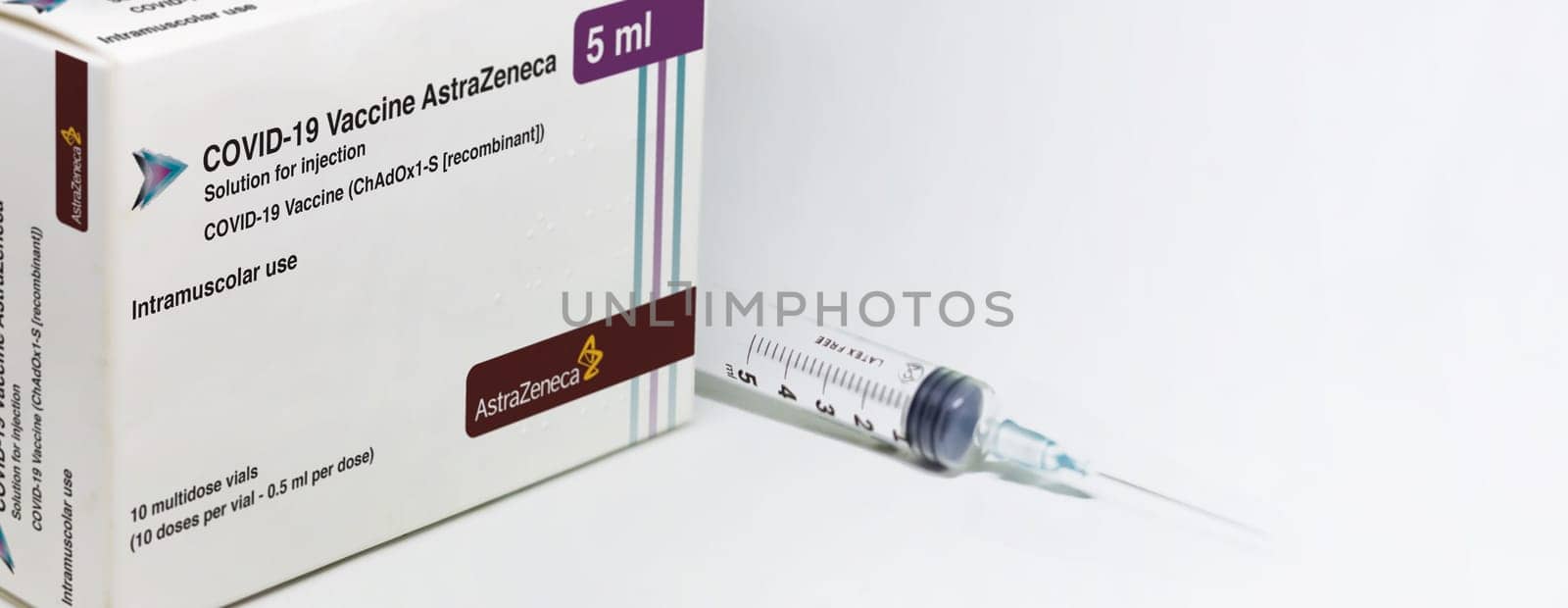 Cambridge, UK, february 5th 2021: A syringe next to the AstraZeneca Covid-19 Vaxzevria vaccine box isolated on a white background. Health and prevention. Copy space and banner. Selective focus