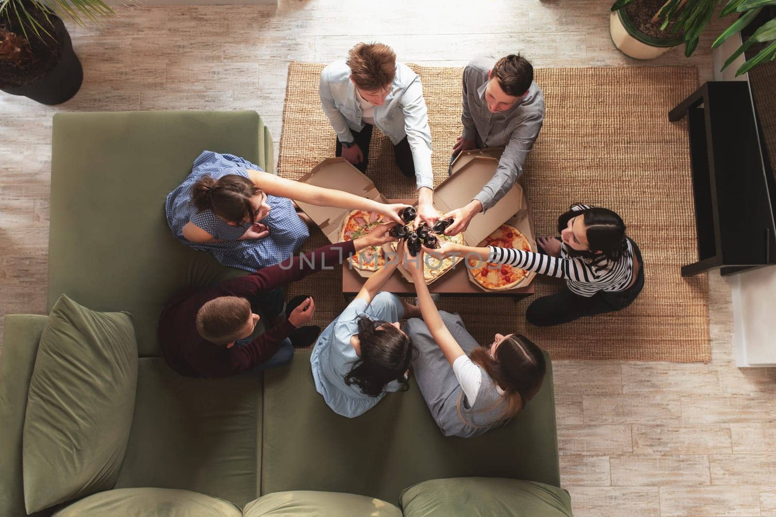 A pizza party, a group of friends chatting and happily eating pizza at the table and drinking sweet soda water. Top view from the second floor. High quality photo