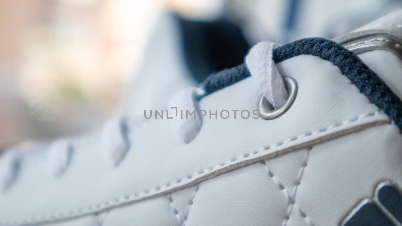White athletic lace-up sneakers. White laces are tied close-up. Blurred background. Sports concept. Metal rivet for shoes as a detail or an element. Fashionable and stylish footwear