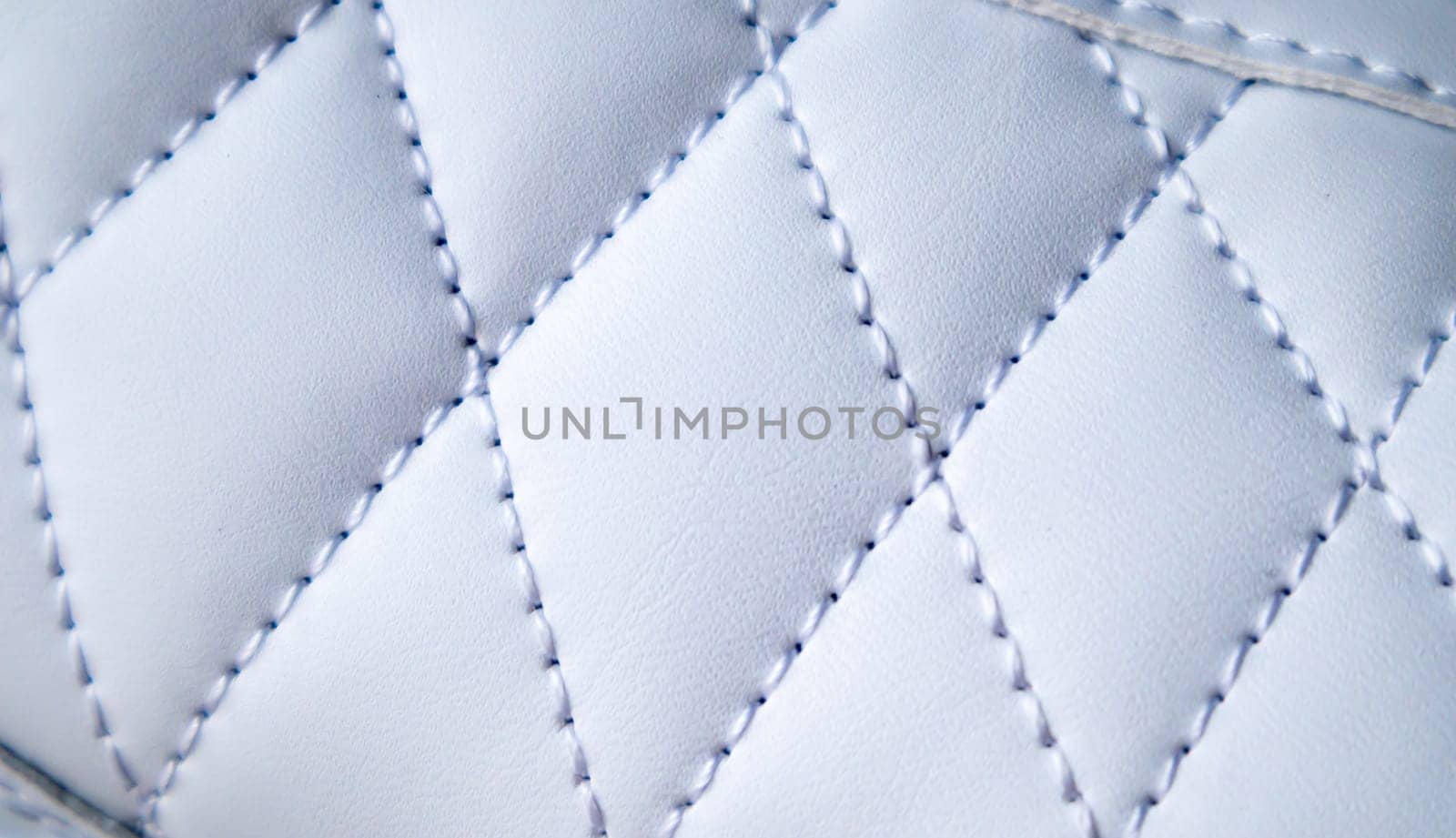 Close-up of synthetic fabric with white diamond stitching. Texture the diamond in a classic style. Luxurious background. Quilted fabric in white or light color, texture