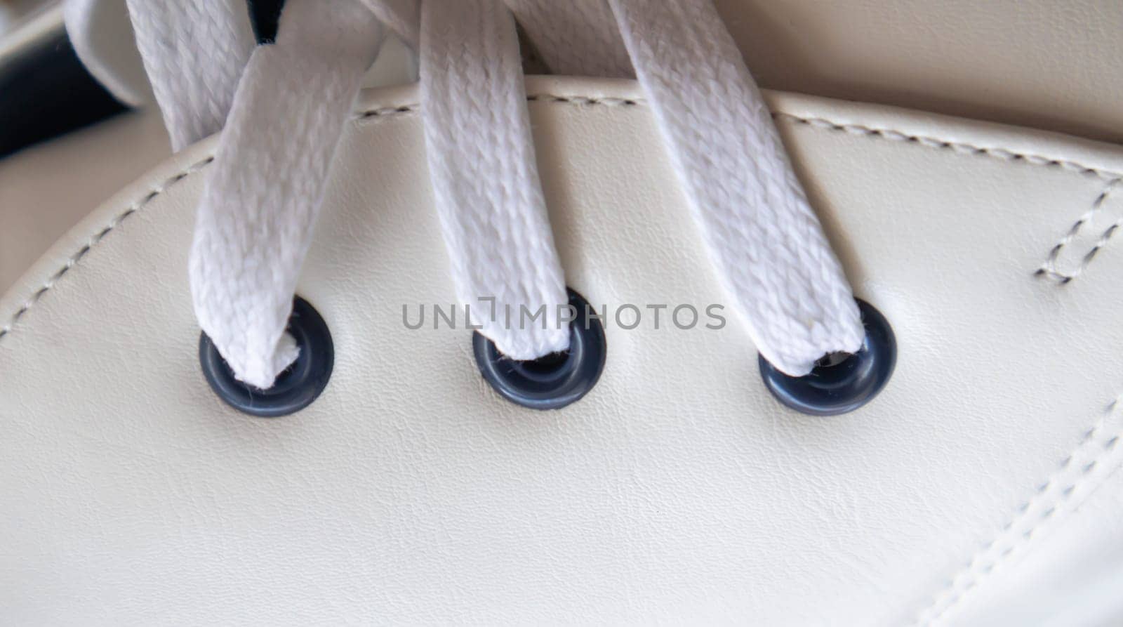 White leather sneakers lace-up shoes. White laces are tied close-up. Blurred background. Sports concept. Metal rivet for shoes as a detail or an element. Fashionable and stylish footwear