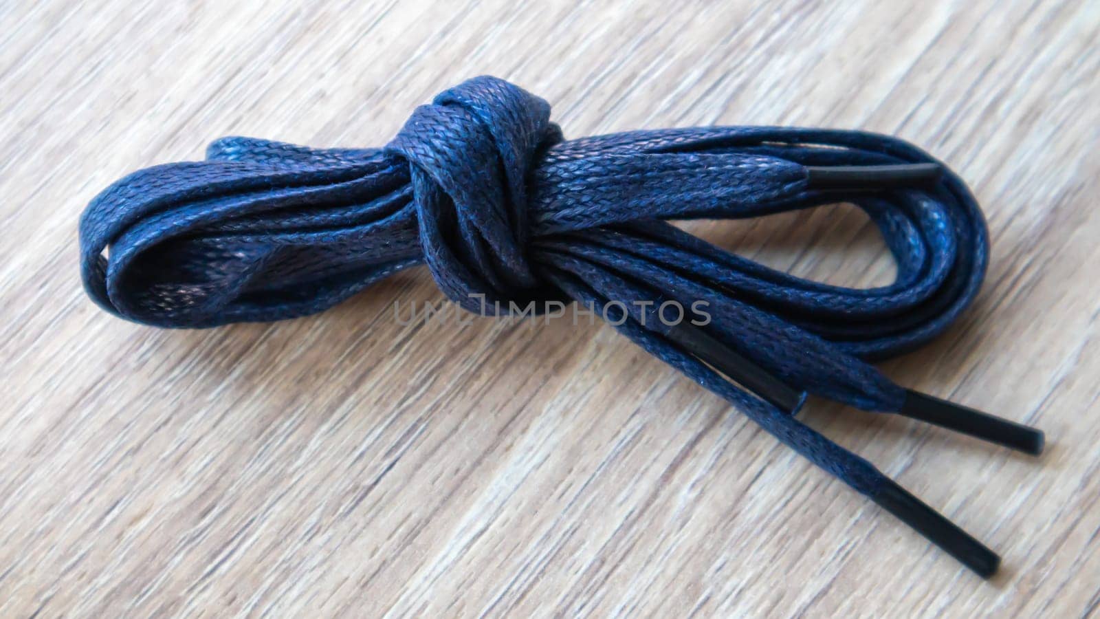 A subject shot of dark blue flat laces with thin tips for shoes rolled up and isolated on a wooden background. Stylish accessory