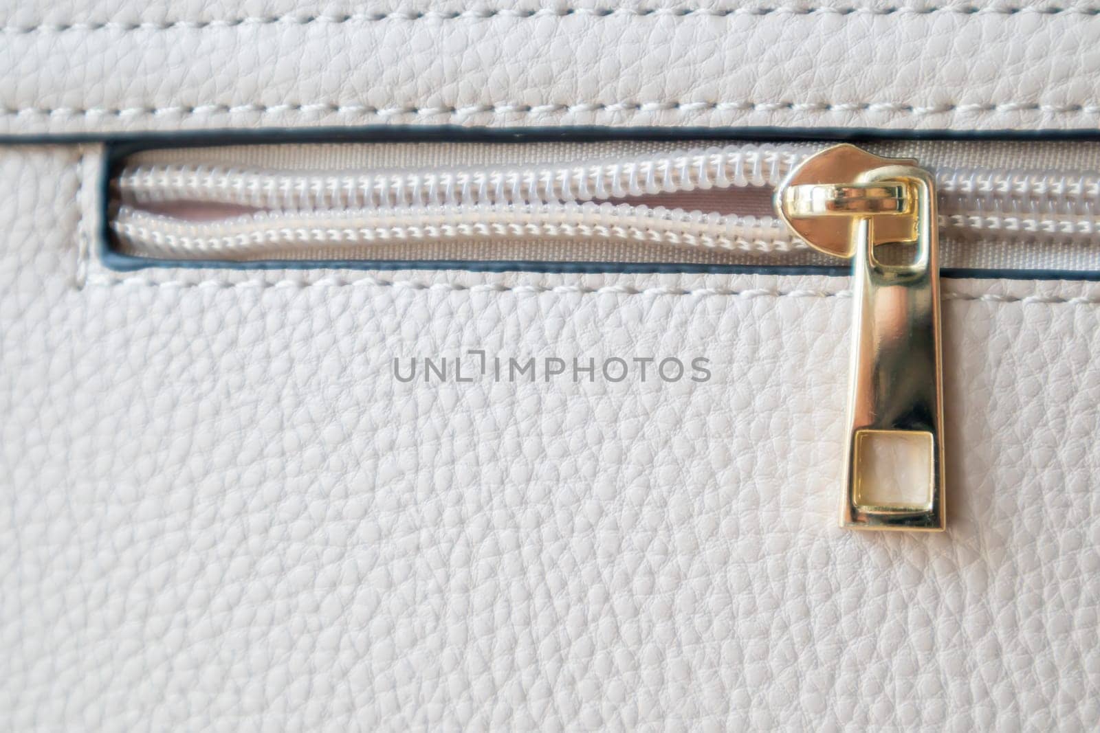 Natural or artificial leather texture. Fragment of a beige or powdery bag with a zipper and stitching. Zipper or clasp bag design element. Bovine skin texture with snake. Macro photo, selective focus