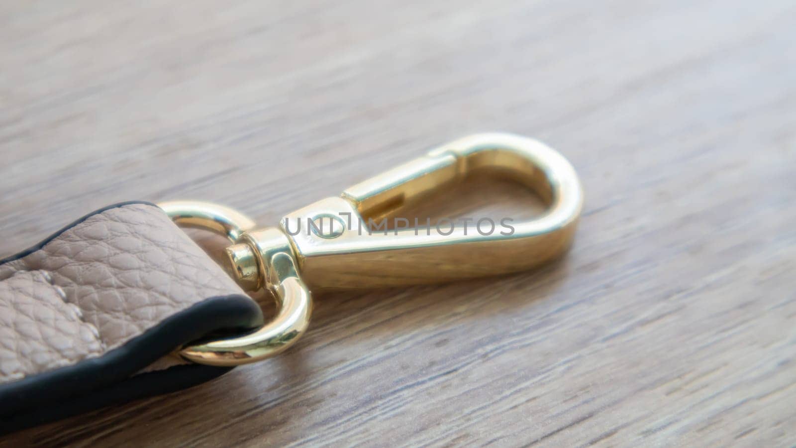 Swivel snap fastener with leather beige bag strap on a wooden background. Metal carabiner with swivel clip or hook. Small gold fittings close-up in selective focus