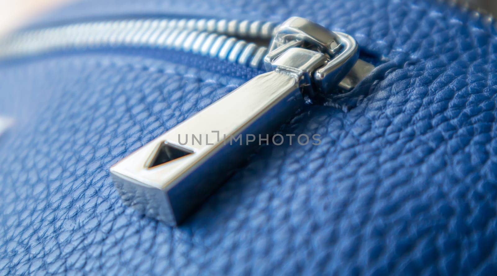 Natural or artificial leather texture. Fragment of a blue bag with a zipper and stitching. Zipper or clasp bag design element. Bovine skin texture with snake. Macro photo, selective focus