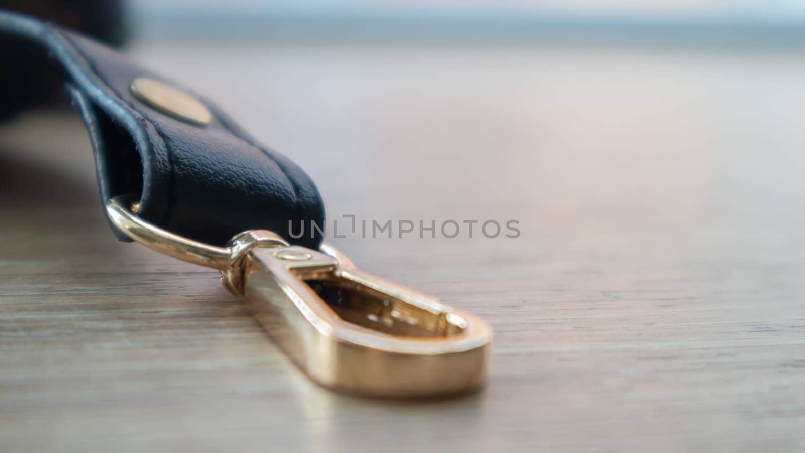 Swivel carabiner fastener with leather black bag strap on a wooden background. Metal carabiner with swivel clip or hook. Small gold fittings close-up in selective focus