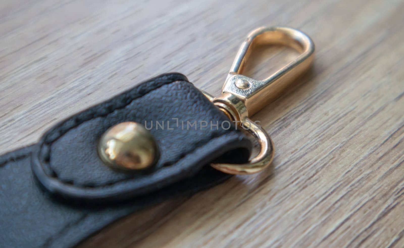 Swivel carabiner fastener with leather black bag strap on a wooden background. Metal carabiner with swivel clip or hook. Small gold fittings close-up in selective focus