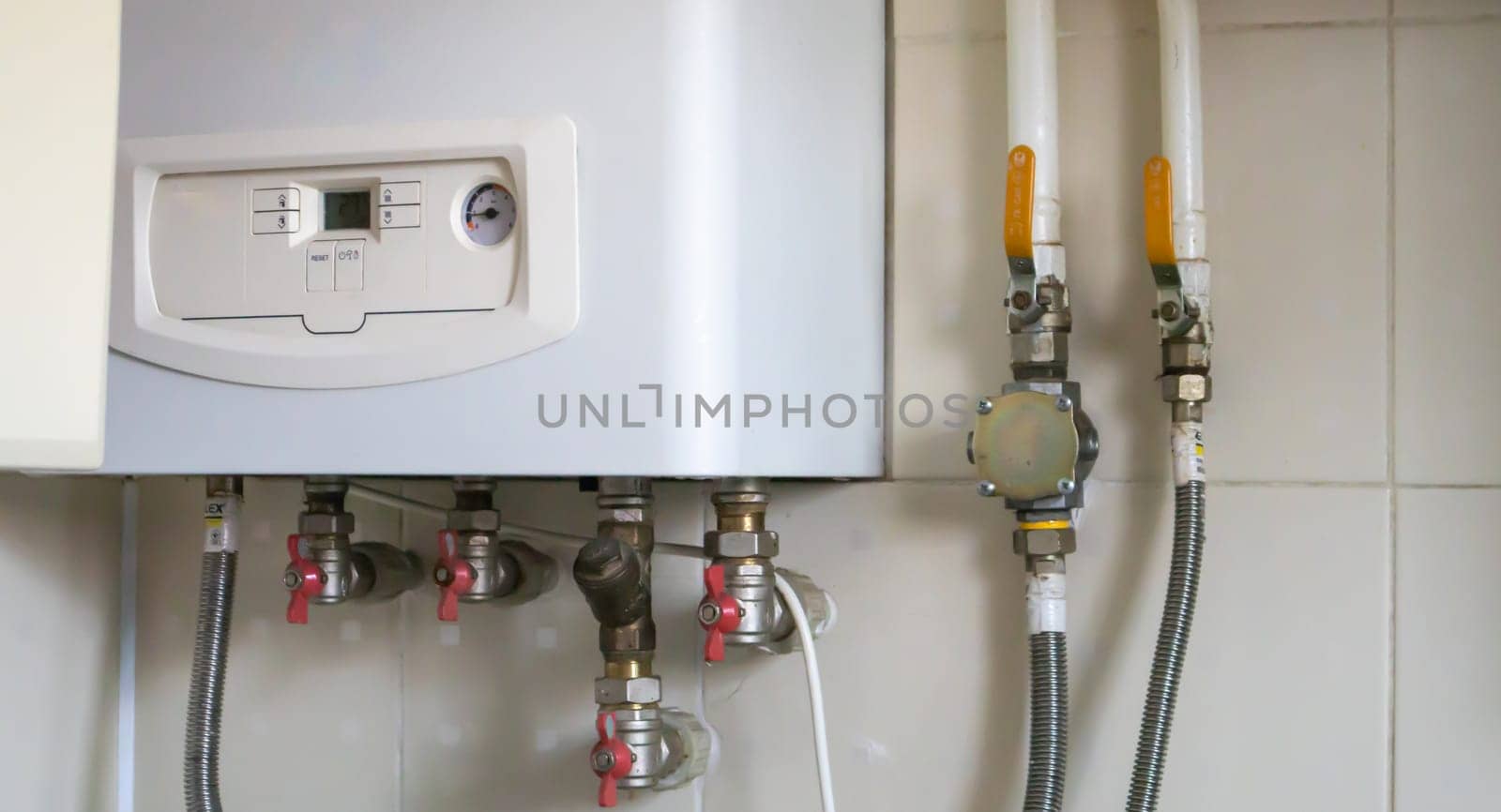 A gas double-circuit boiler is installed in the apartment. Autonomous heating boiler with a control panel, buttons, a display with temperature readings and red valves on pipes in a home kitchen