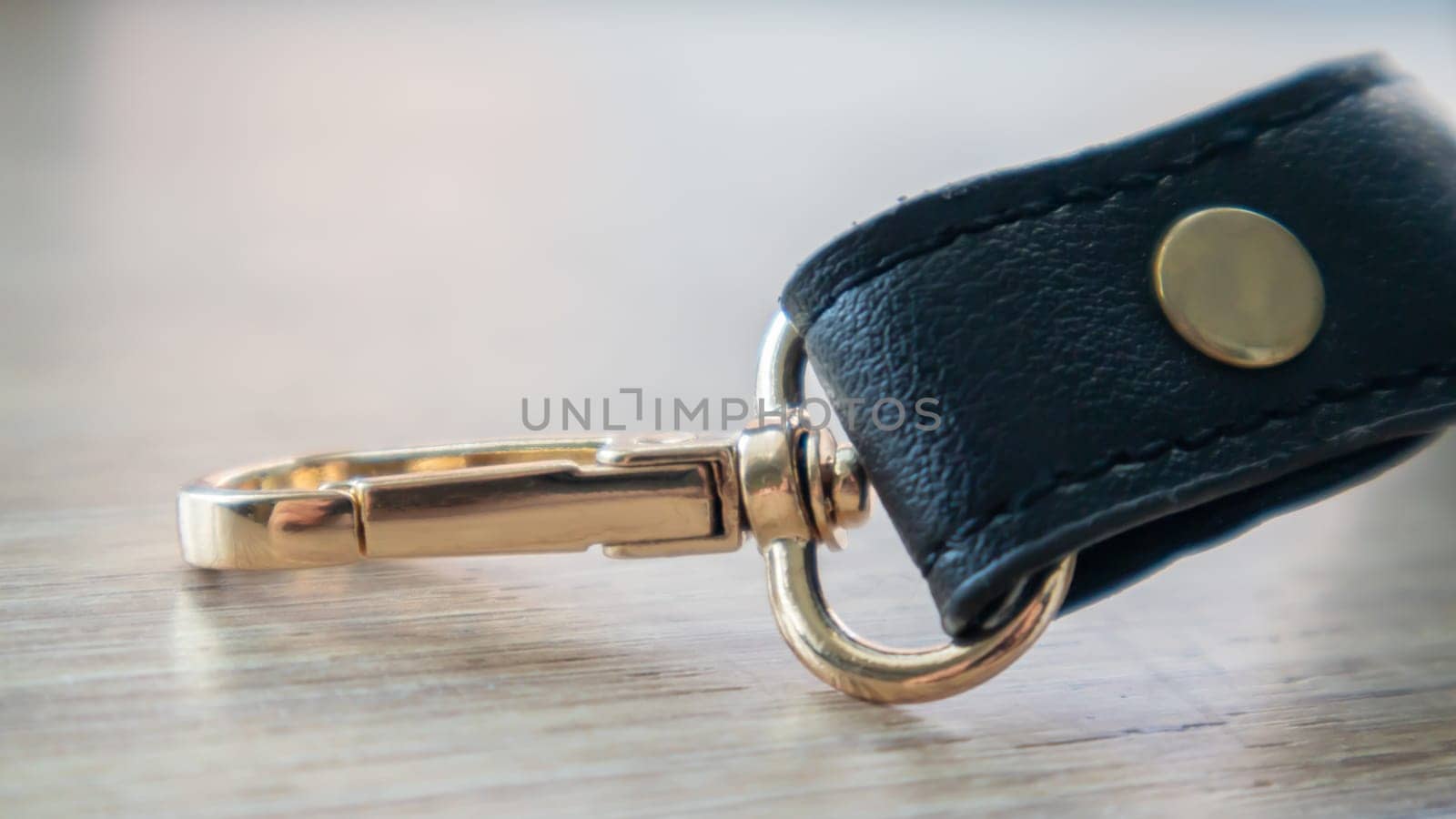 Swivel carabiner fastener with leather black bag strap on a wooden background. Metal carabiner with swivel clip or hook. Small gold fittings close-up in selective focus