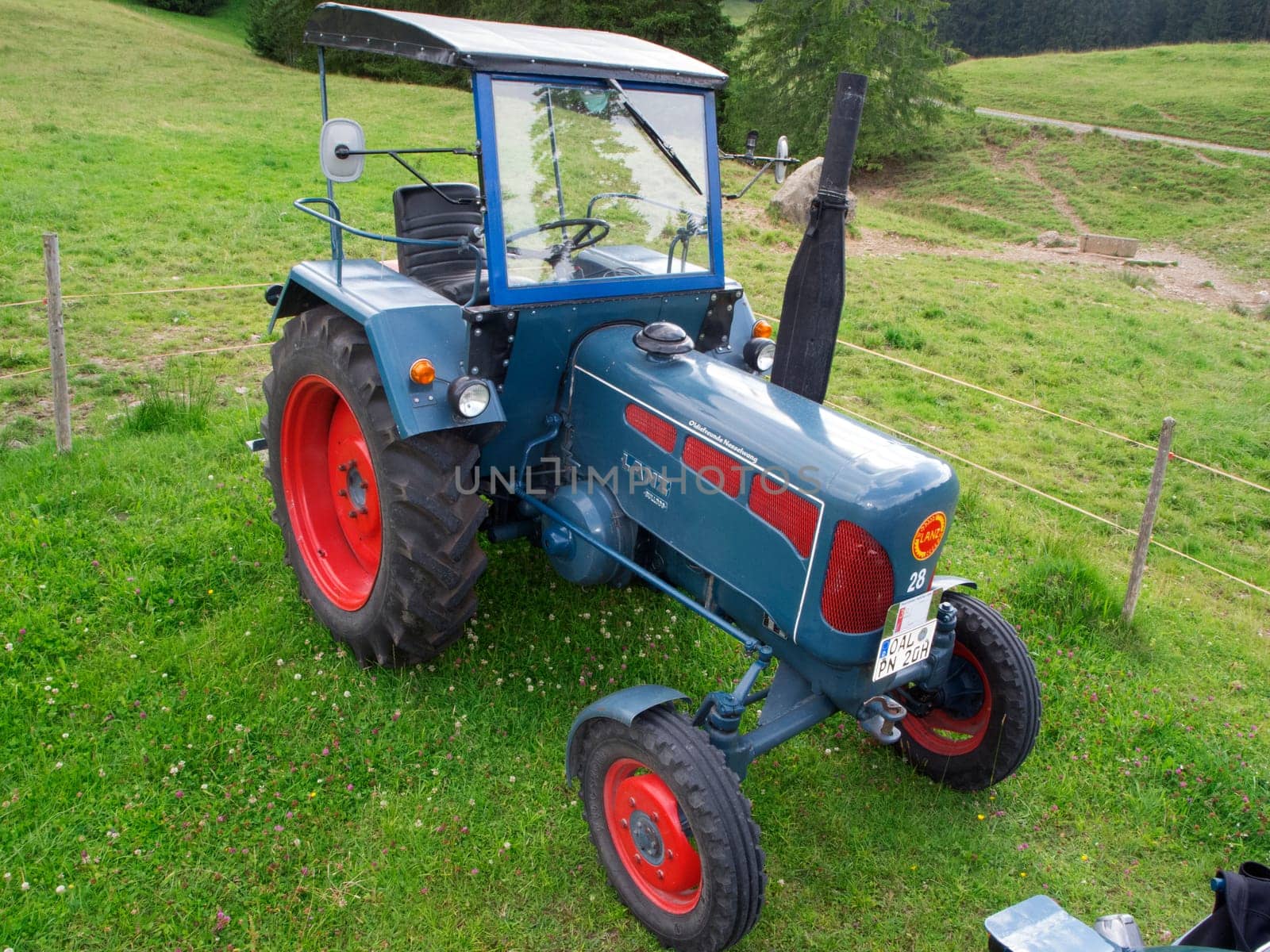Nesselwang, Germany - July 23, 2020: Side view of a blue perfectly restored LANZ tractor away from a veteran tractor right on a green meadow.