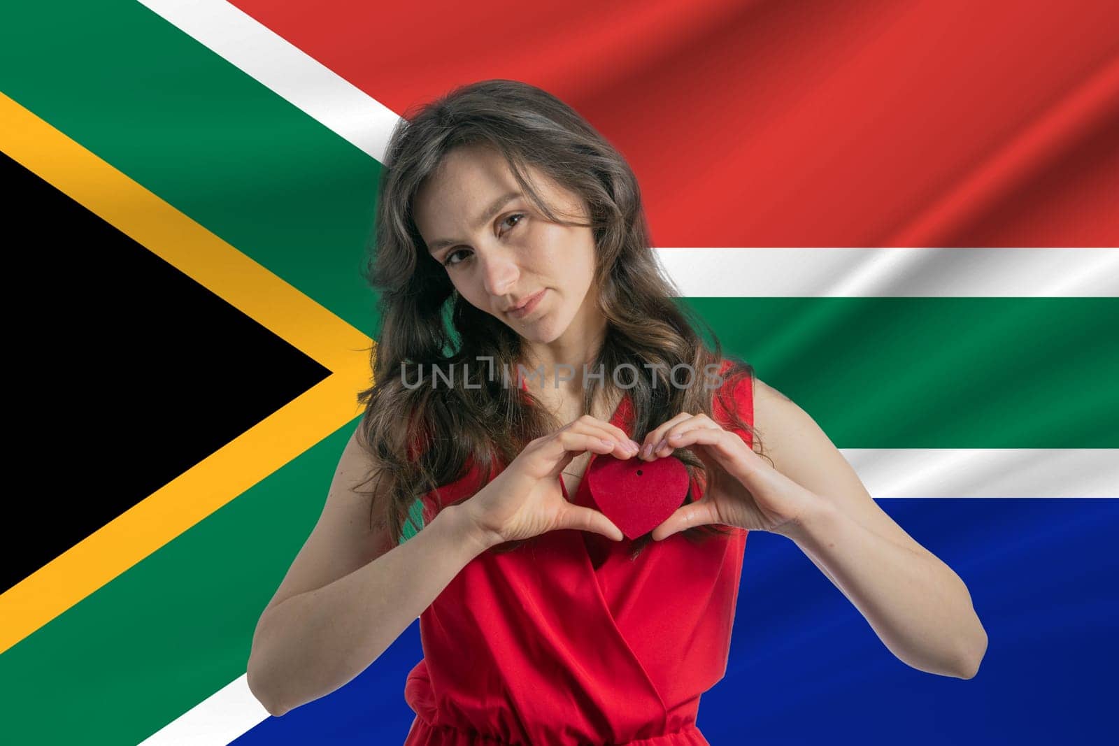 Love South African Republic. A girl holds a heart on her chest in her hands against the background of the flag of South African Republic. The concept of patriotism.