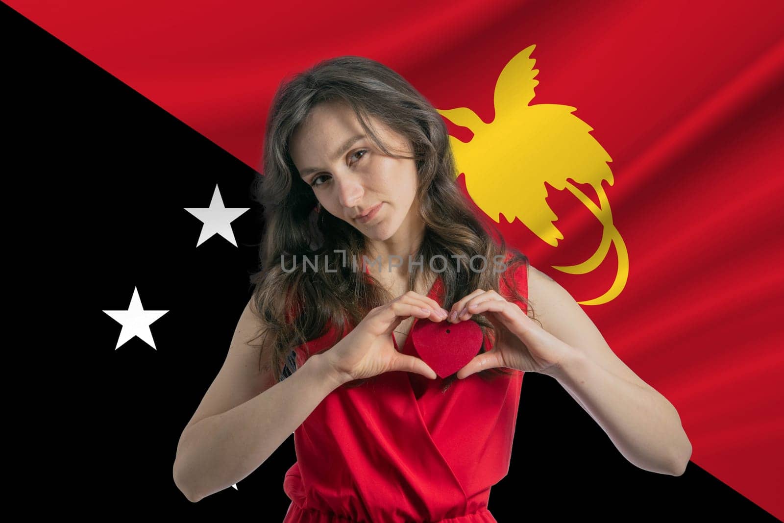 Love Papua New Guinea. A girl holds a heart on her chest in her hands against the background of the flag of Papua New Guinea. The concept of patriotism.