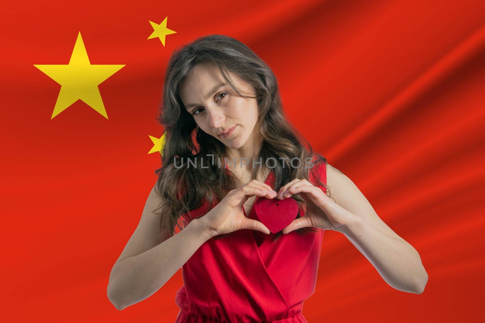 Love People's Republic of China A girl holds a heart on her chest in her hands against the background of the flag