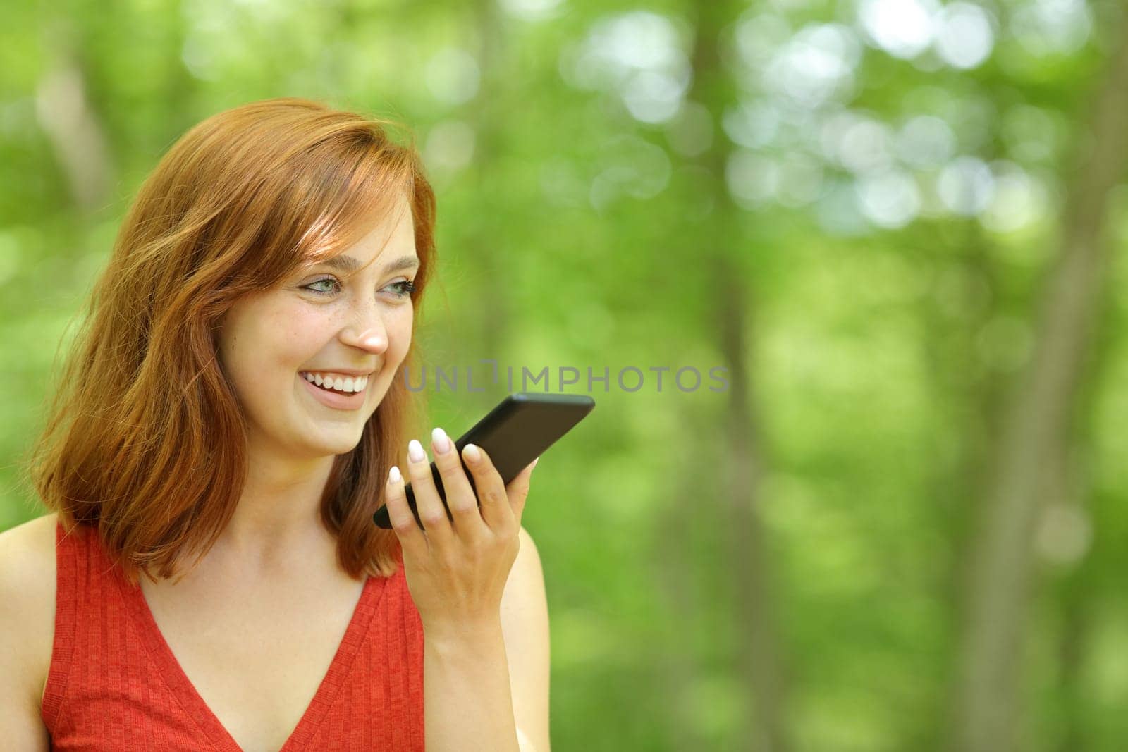 Happy woman using voice recognition on phone in a forest