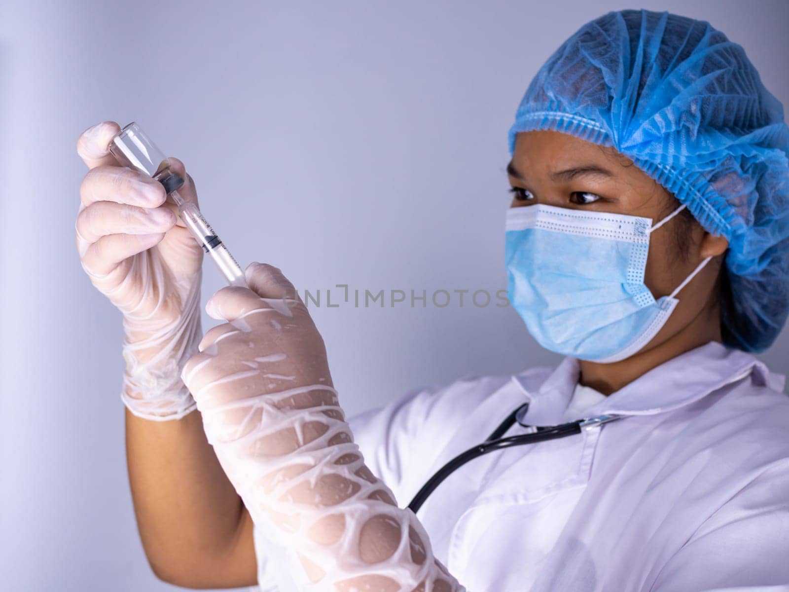Studio portrait of a female doctor wearing a mask and wearing a hat. In hand was a bottle of vaccine and a sling of syringes. standing on a white background. Studio shot background, COVID-19 concept