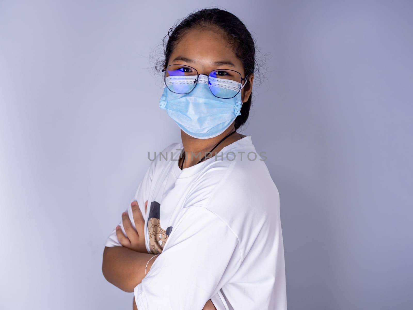 girl wearing a mask and wearing glasses standing with arms crossed on a white background