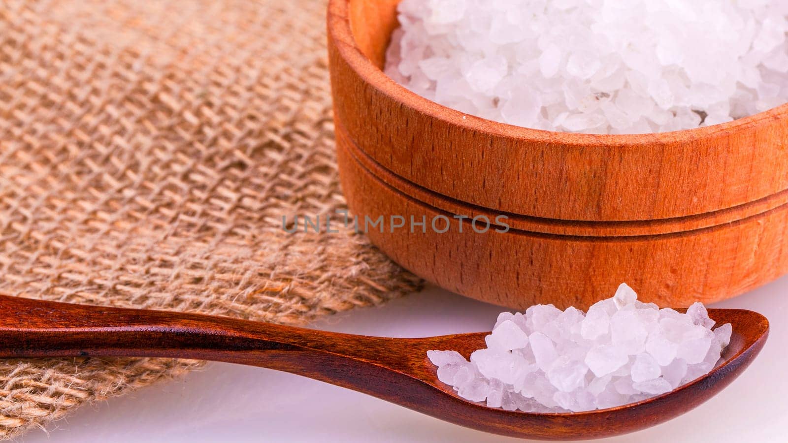 The wooden cup and spoon with a white bath salt on burlap on white background
