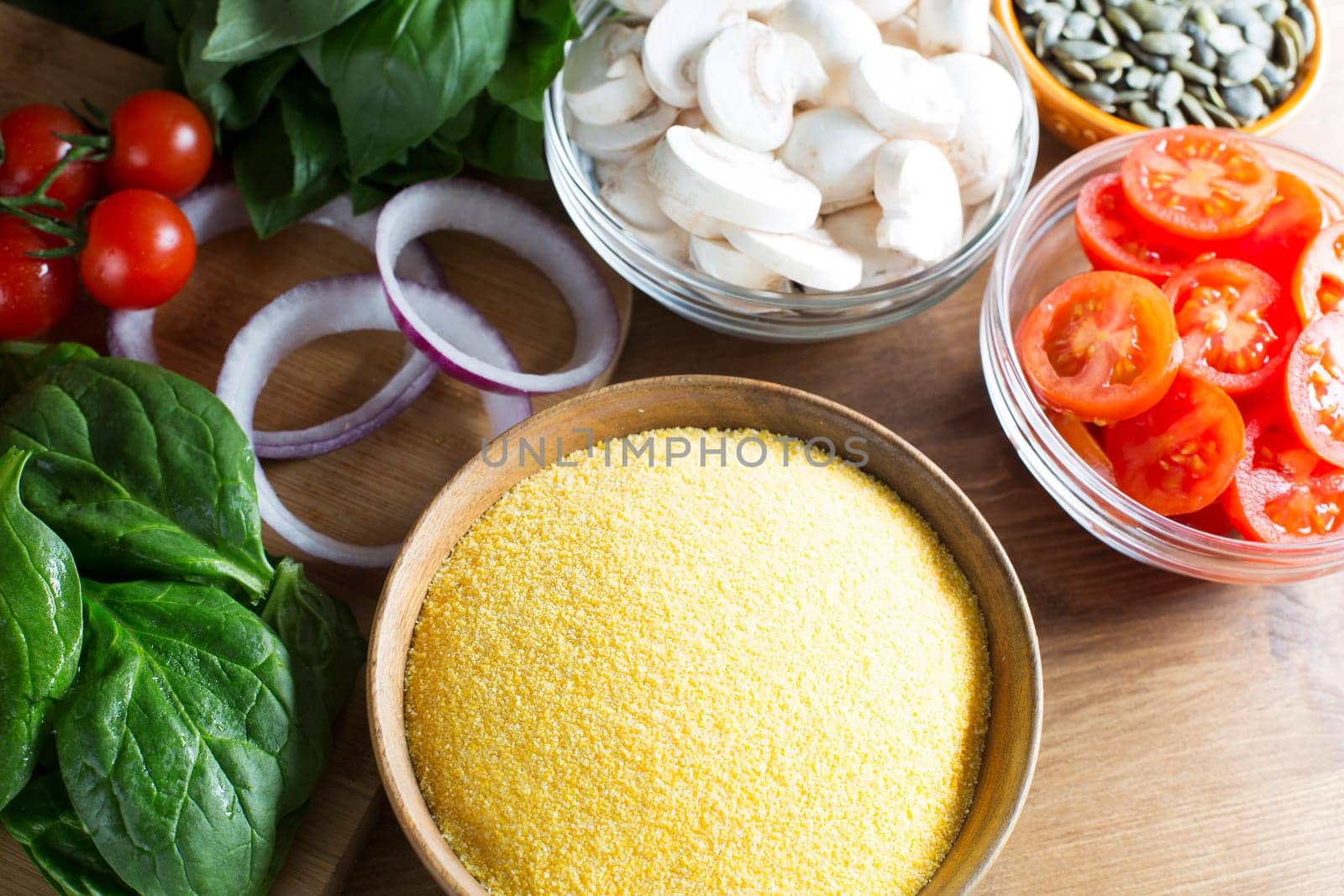 Ingredients for polenta recipe, with polenta in wooden bowl with sliced tomatoes, spinach and red onions.