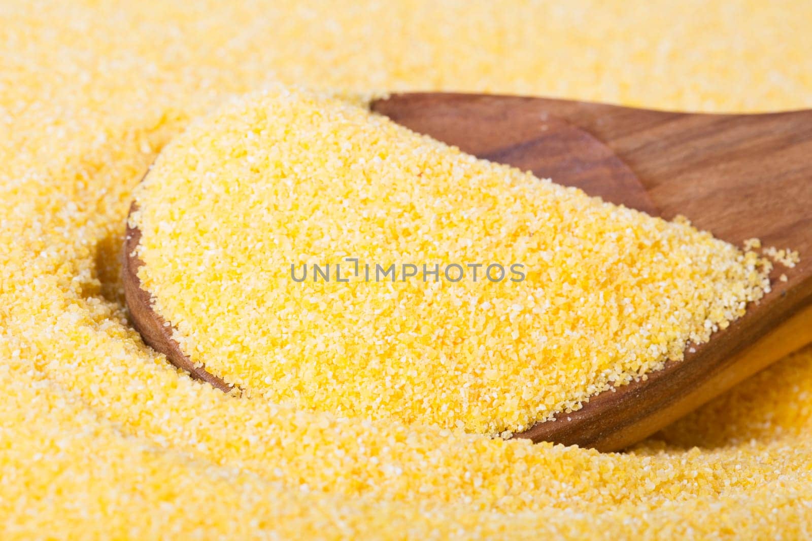 Close up of wooden spoon in raw polenta.
