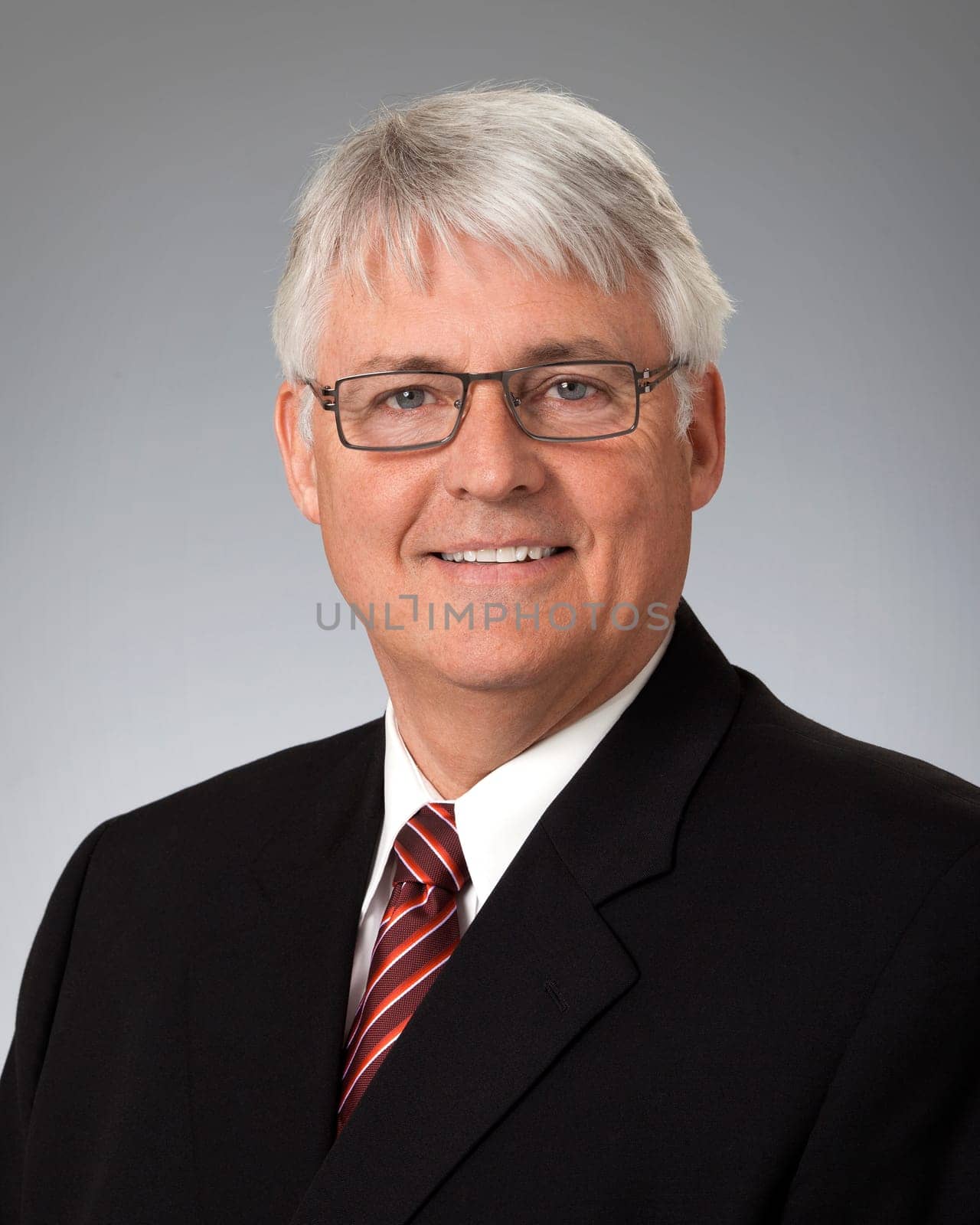 Studio portrait of mature businessman wearing black suit, against a gray background.