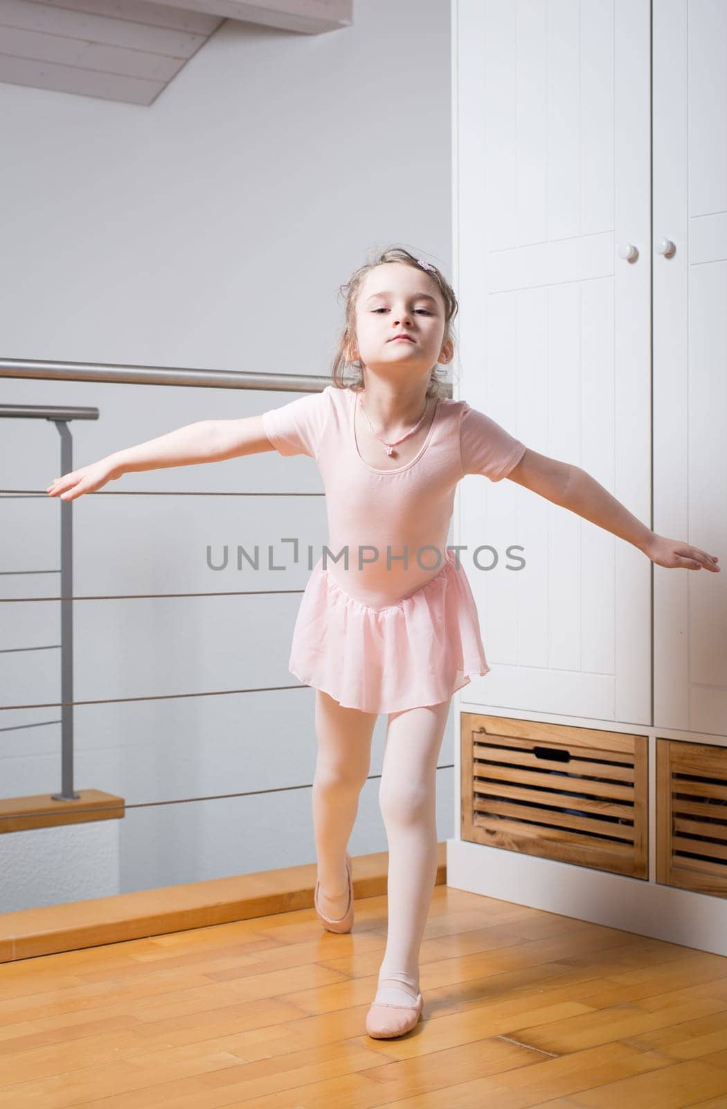 Little girl wearing a ballet dress is practicing ballet in a dance studio
