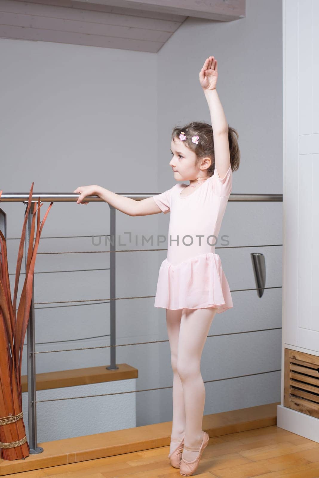 Little girl wearing a ballet dress is practicing ballet in a dance studio