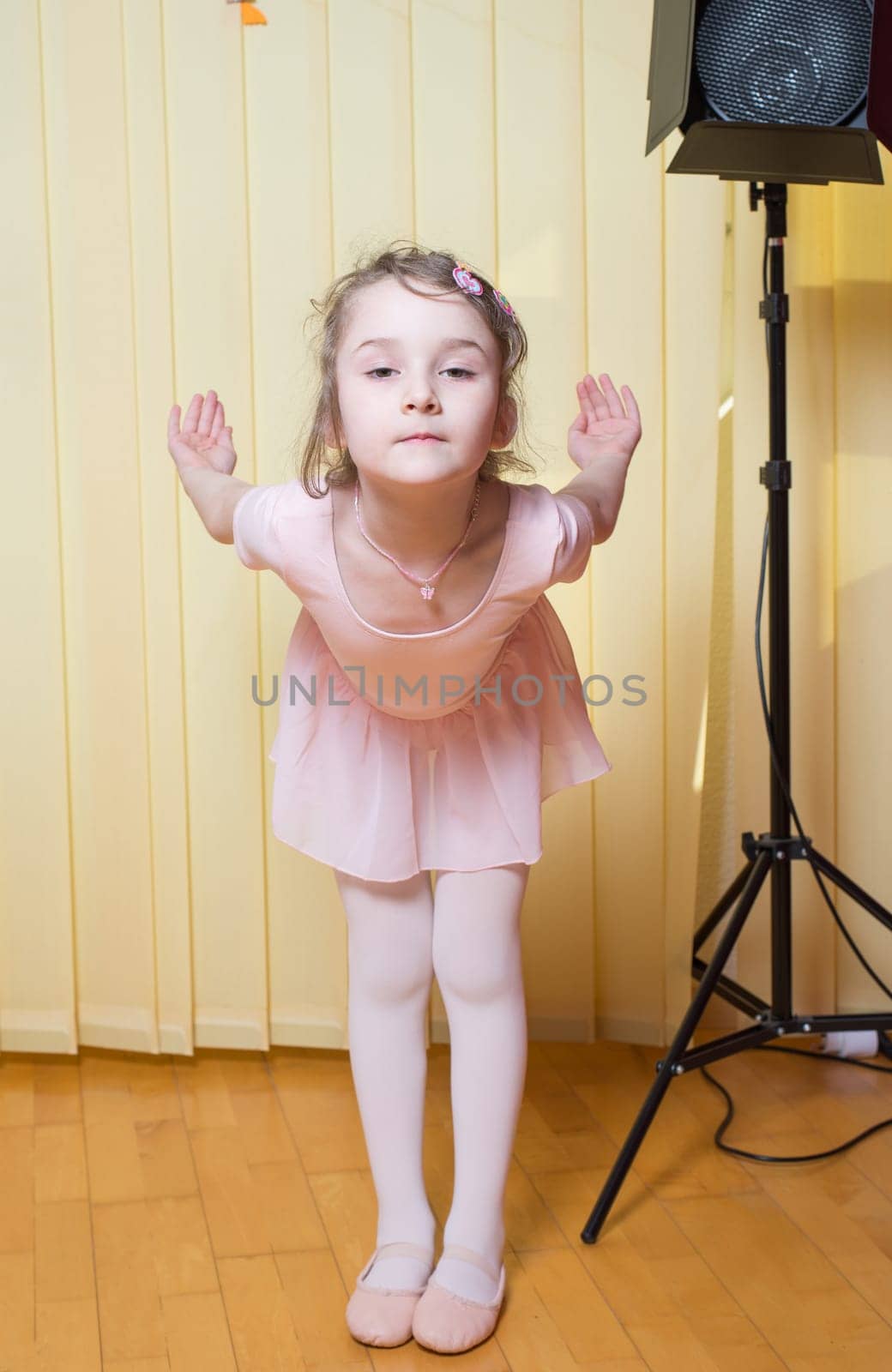 Little girl wearing a ballet dress is practicing ballet in a dance studio