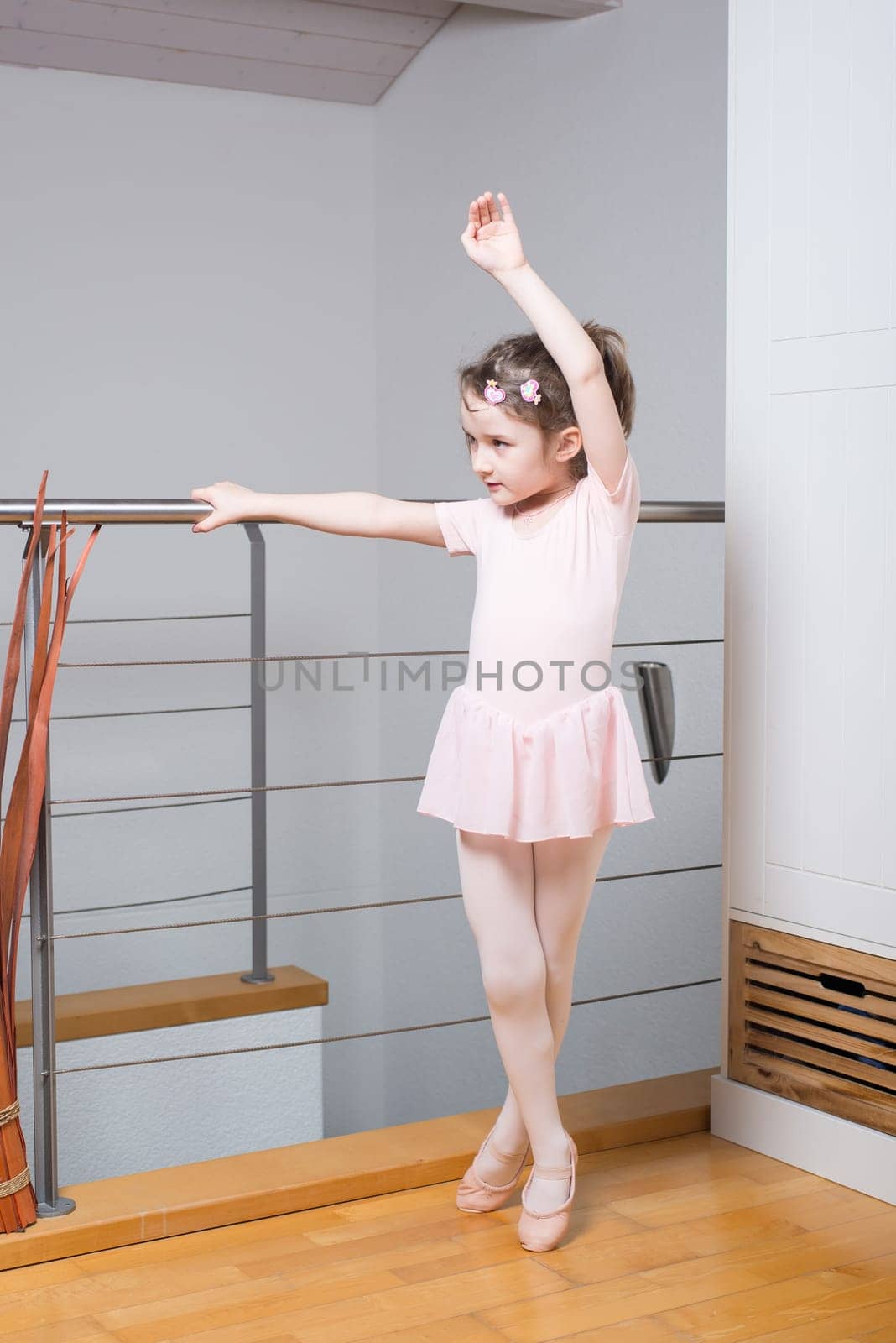 Little girl wearing a ballet dress is practicing ballet in a dance studio