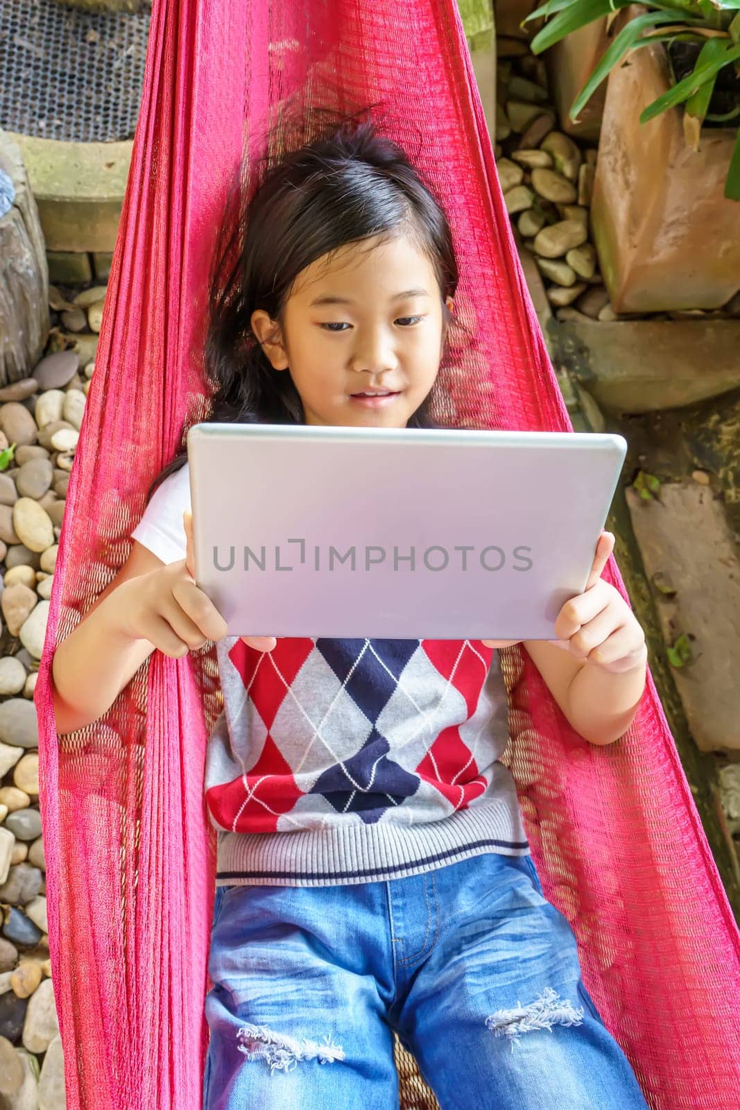 The girl lying in hammock with playing tablet pc.