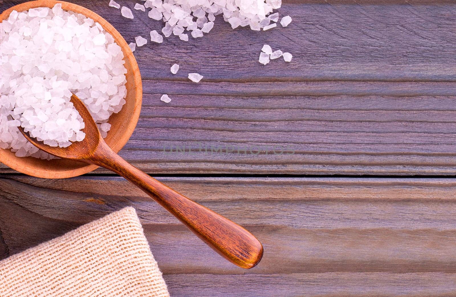 The white sea salt on cup, spoon and burlap on a wooden table