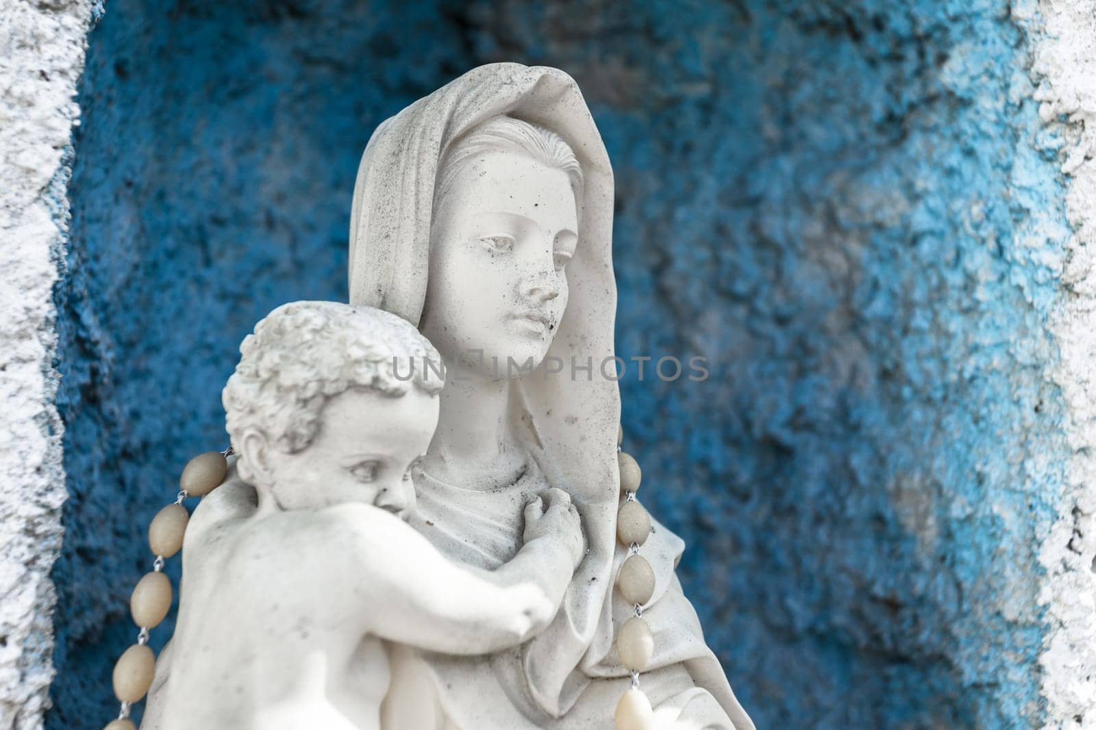 Statue of Our lady of holy rosary and child Jesus. Blue rustic concrete on background.