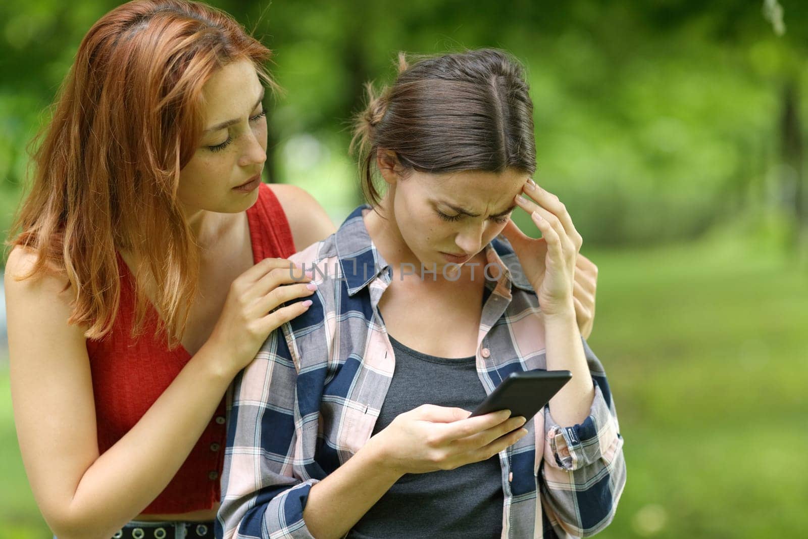 Sad student checking phone being comforted by a friend