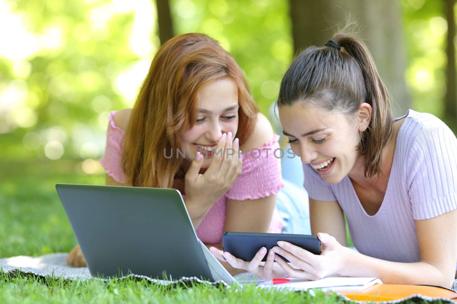 Happy students watching videos on smart phone in a park