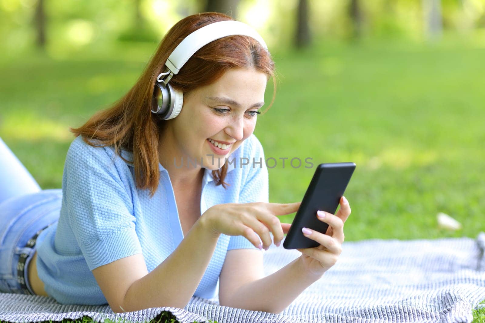 Happy woman listening to music checking phone in a park