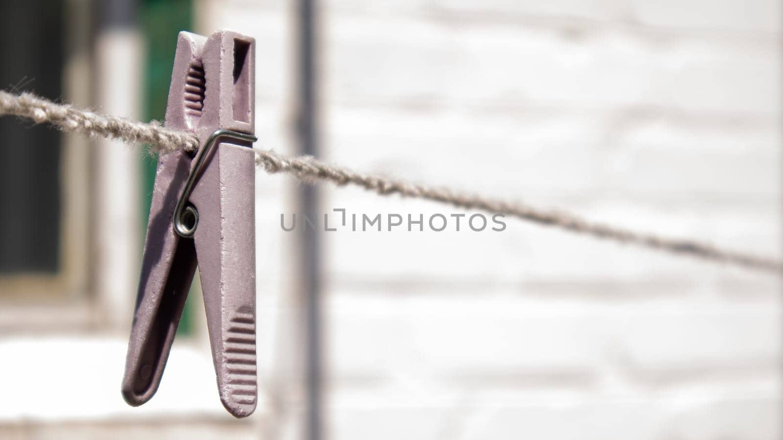 Plastic clothespins hang in a row on the rope. Rope outdoors, on a blurred background in a sunny garden. Clothesline on the street. Clothespins