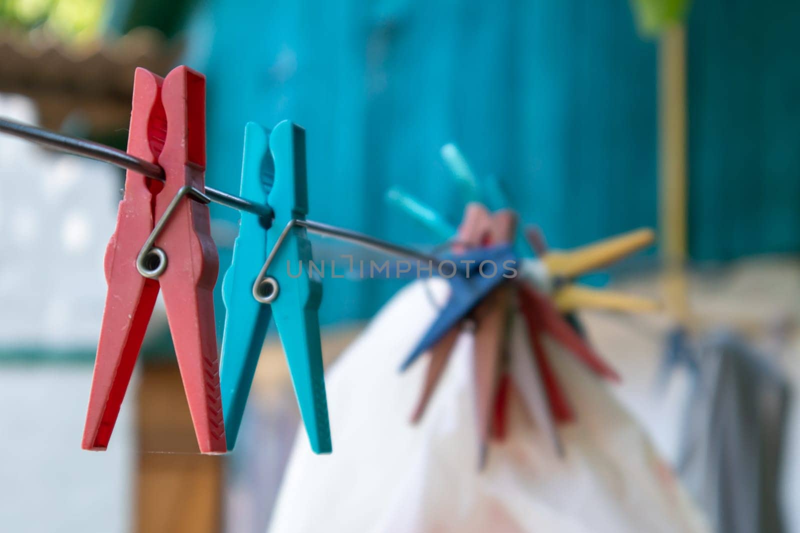 Plastic clothespins hang in a row on the rope. Rope outdoors, on a blurred background in a sunny garden. Clothesline on the street. Clothespins