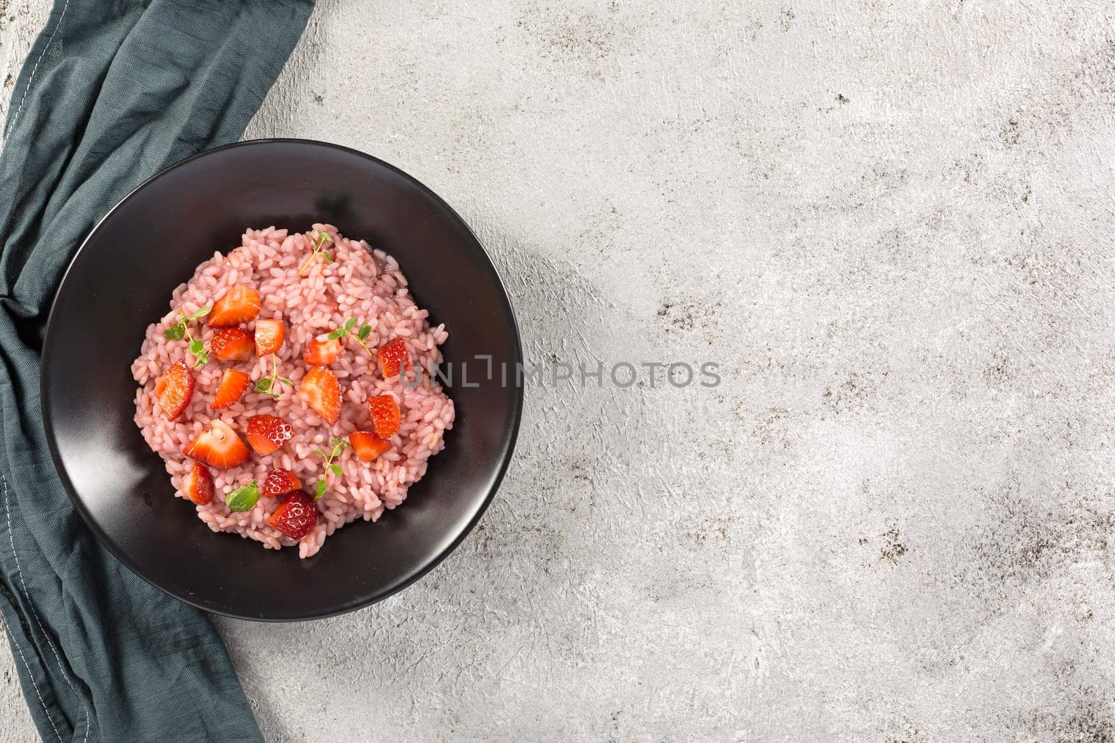 Risotto with strawberry fruits served in a black dish on a grey stone table. flat lay with copy space. Italian gourmet cuisine. Selective focus.