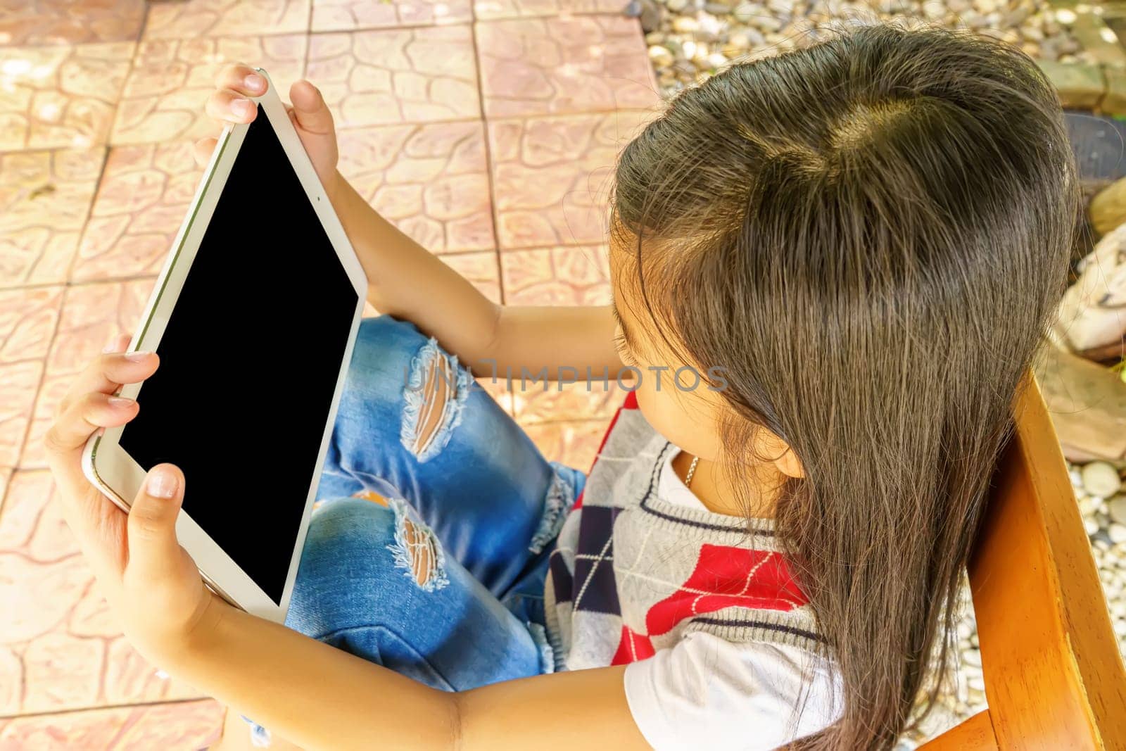 The girl sitting on wooden chair with playing tablet pc.