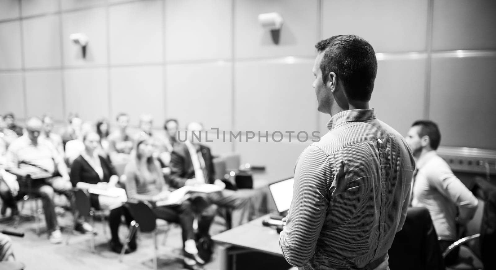 Speaker giving a talk on corporate business conference. Unrecognizable people in audience at conference hall. Business and Entrepreneurship event. Black and white.